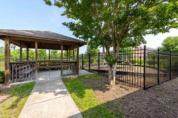 A gazebo is surrounded by a black fence and a tree.
